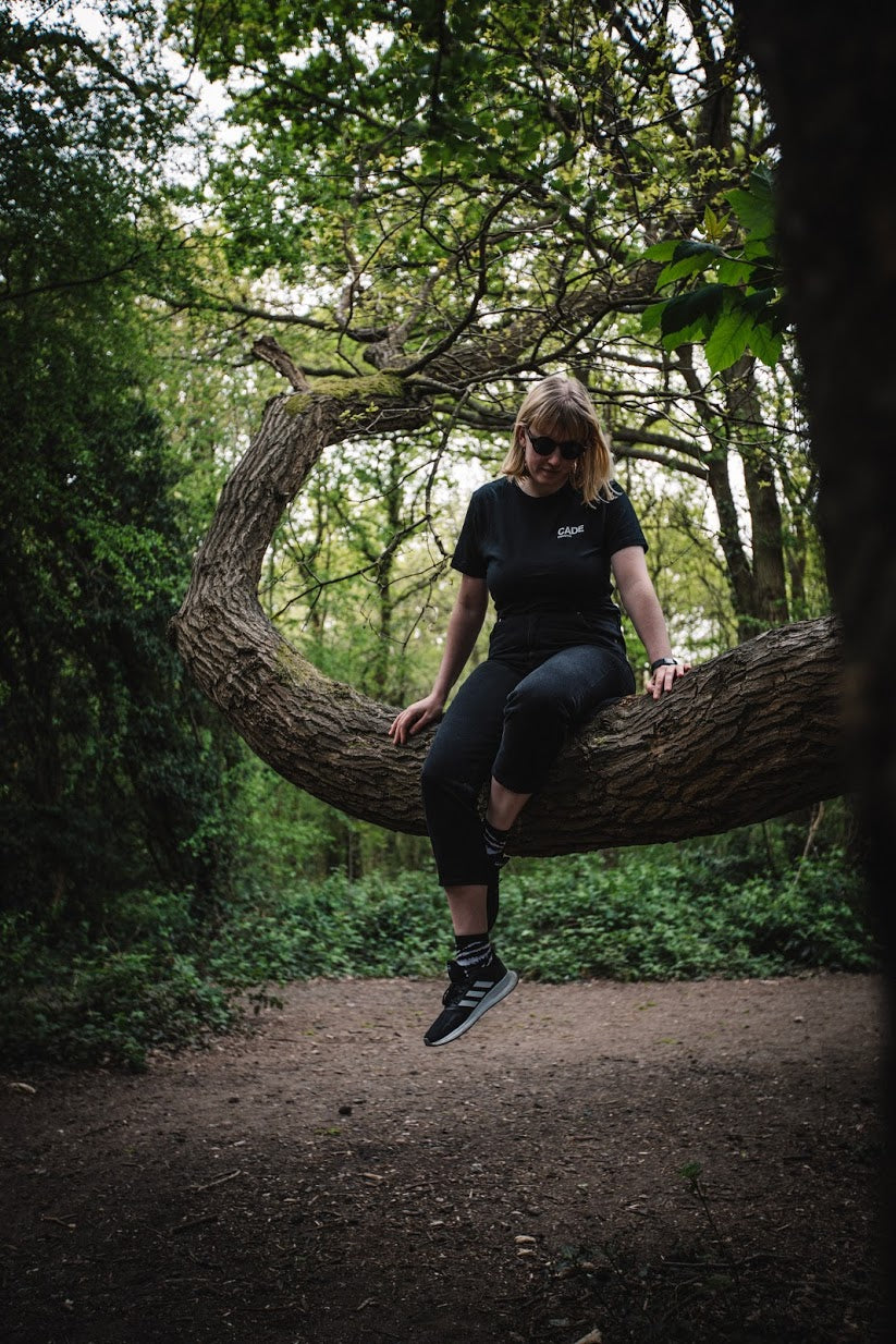 LADY sitting on a tree looking into the distance wearing the new CADE t-shirt
