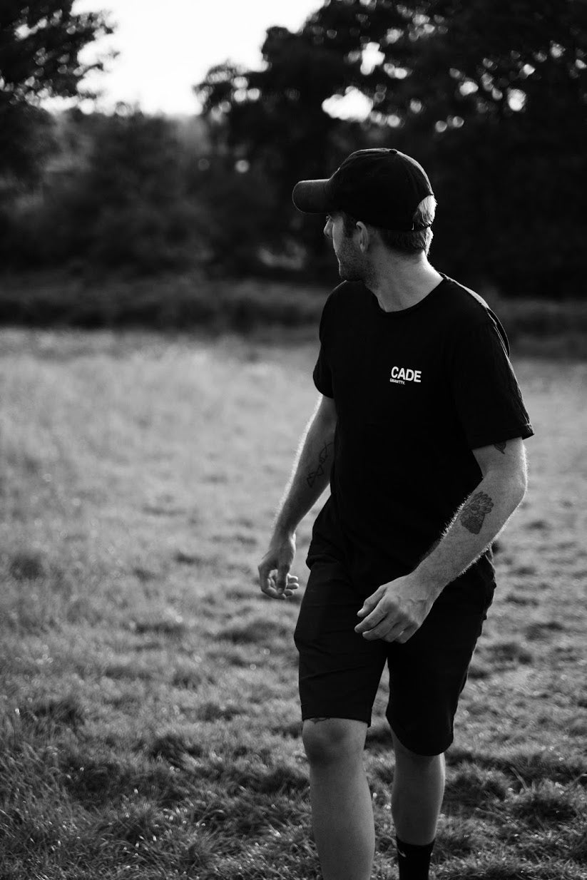 Francis Cade walking in a park looking into the distance wearing the new black CADE t-shirt with white logo