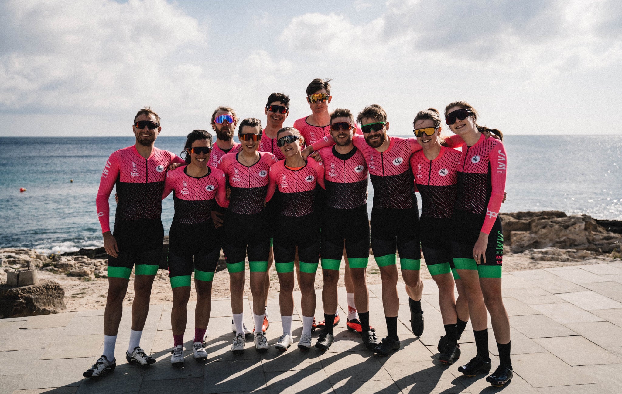Group of JAM Cycling race team wearing racing skinsuits in the sunshine by the beach on training camp in spain