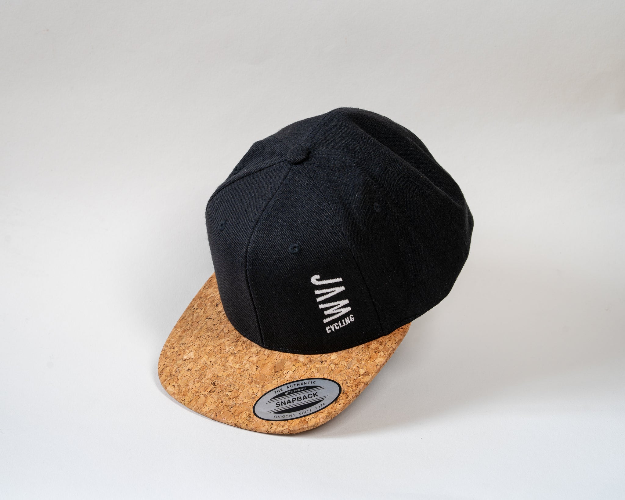 JAM snap back cap featuring cork peak stitched JAM logo floating on a white background cool product photography