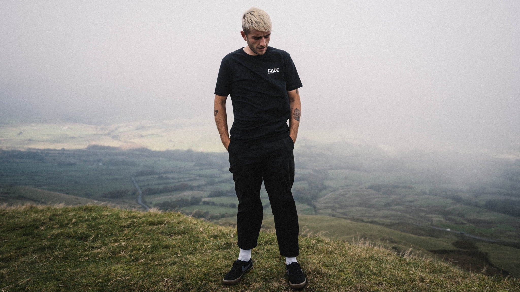 Francis Cade stood on a hill in the PEAK district looking into the distance wearing the new CADE t-shirt